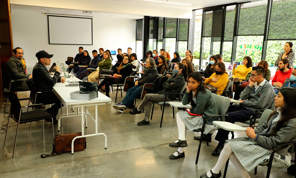 Foto de una salón de clases donde se encuentran varios estudiantes jóvenes y dos profesores al frente