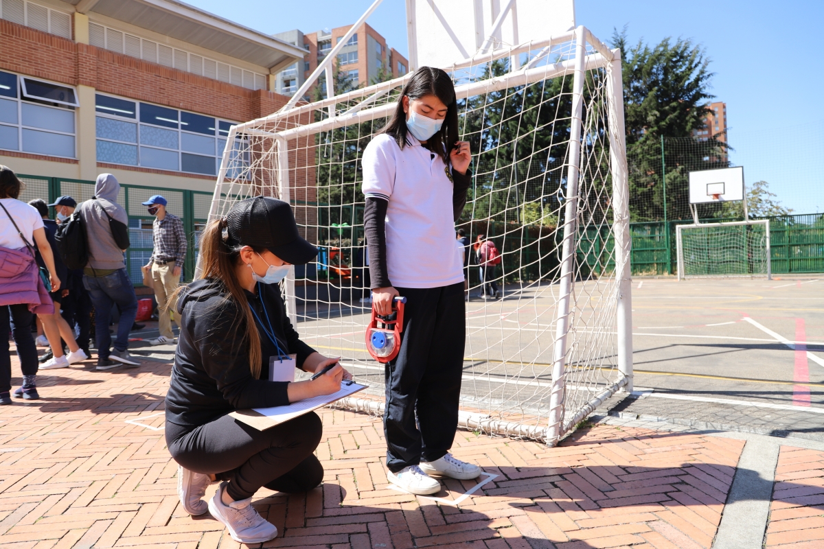 Foto de una mujer tomando medidas a una estudiante en una cancha de micro futbol