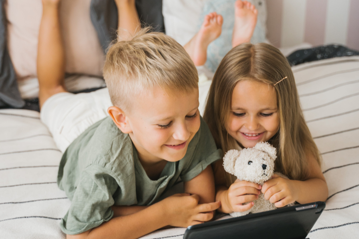 una niña y un niño en la cama viendo contenido en una Tablet