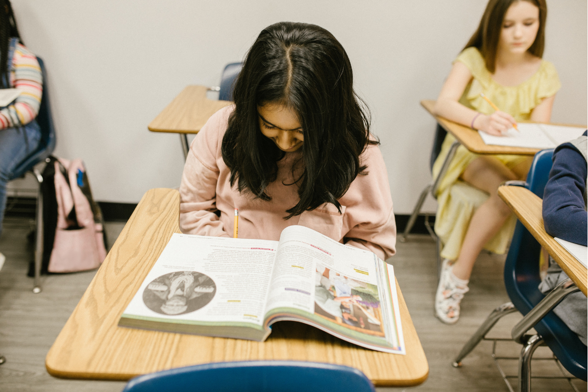 Foto de una estudiante leyendo, sentada en su pupitre