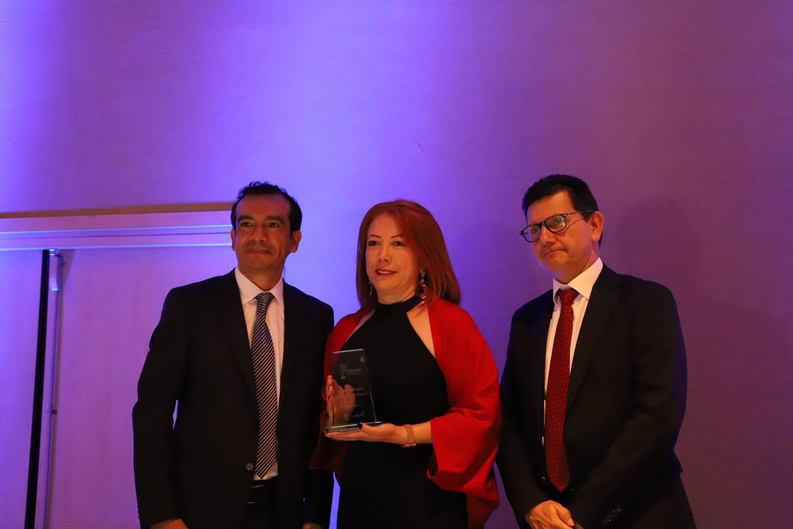 Foto de una docente recibiendo el premio, a su lado el Director del Idep y el Subsecretario de la SED