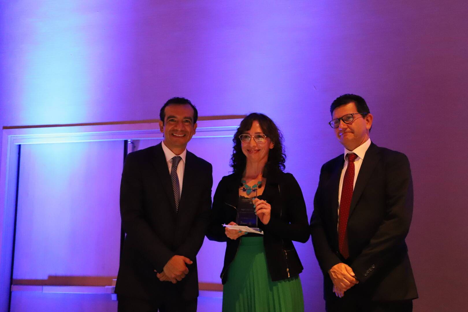 Foto de una profe recibiendo el premio, a su lado el Director del Idep y el Subsecretario de la SED