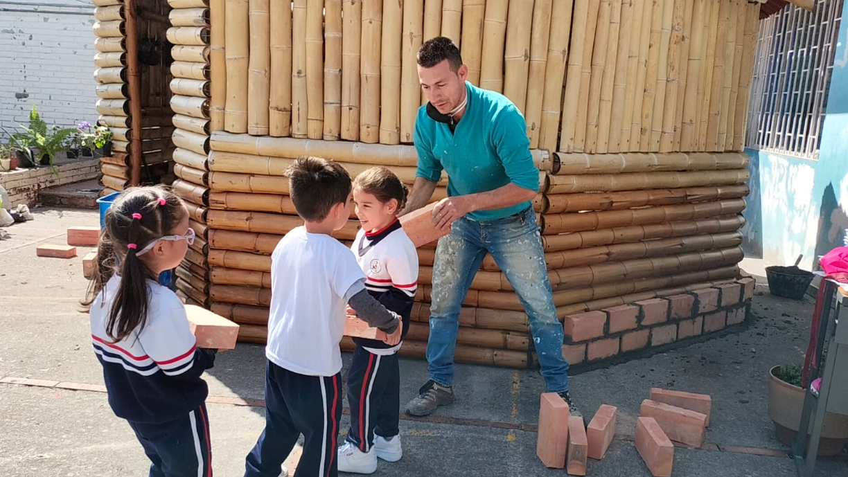 Niños recibiendo unos ladrillos junto a una cabañita en guadua