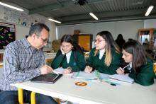 Foto de un profesor haciendo una explicación en una mesa a 3 estudiantes mujeres