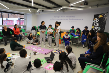 Foto de un salón de clase donde están reunidos varios estudiantes y acudientes viendo una cartelera que se encuentra en el suelo.