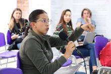 Foto de una maestra hablando por micrófono en un aula